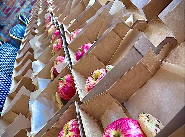 Rows of brown-paper boxed lunches with apples and cookies