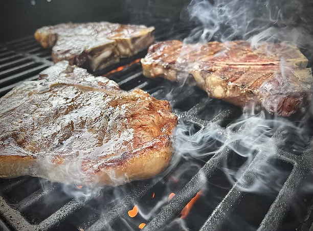 Ribeye steaks searing on a hot grill with smoke and flames